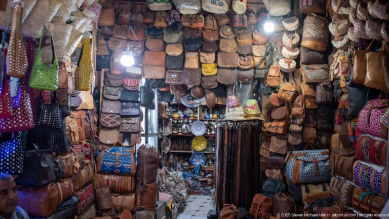 Compact souk shop with walls and ceiling densely hung with leather bags, pouches, wallets, and decorated satchels.
