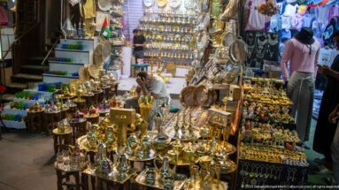 Souk shop packed with polished brass-colored trays, teapots, lamps, pitchers, and decorative metal vessels.