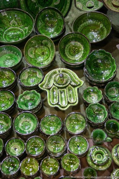 Green-glazed ceramic plates, bowls, and serving pieces arranged closely together around a hand-shaped dish.