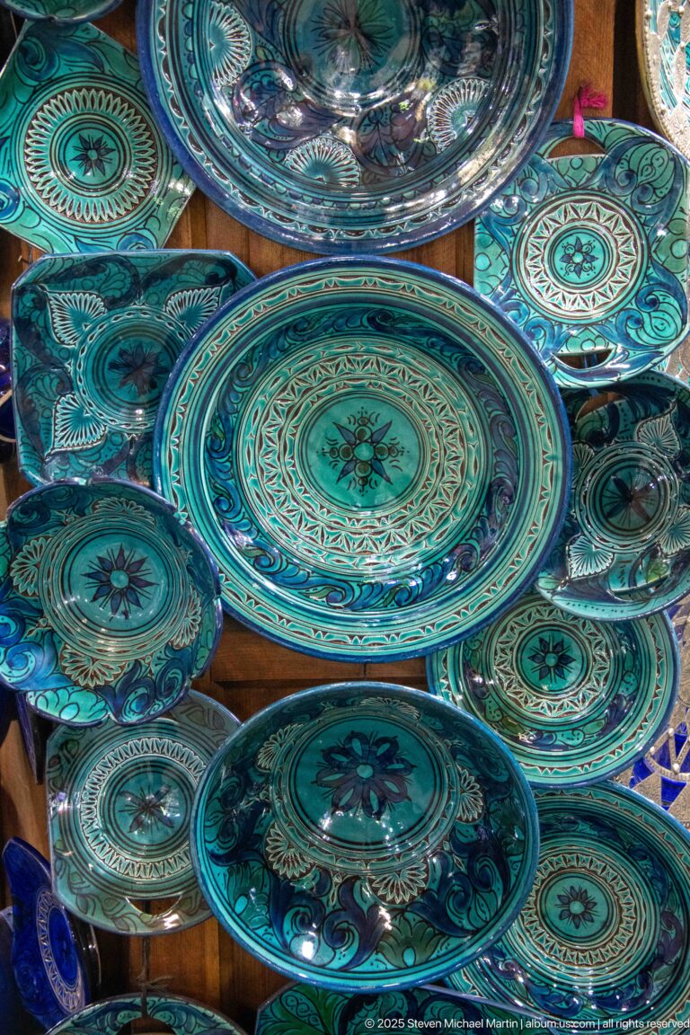 Overlapping turquoise and blue-green ceramic plates decorated with radial floral and geometric patterns in a market display.