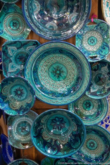 Overlapping turquoise and blue-green ceramic plates decorated with radial floral and geometric patterns in a market display.