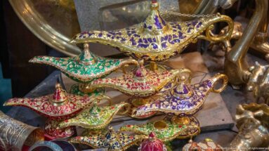 Small decorative metal oil-lamp souvenirs with curved spouts, handles, and colorful jeweled or enamel-like ornament.