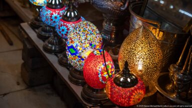 Glowing multicolored mosaic-glass table lamps beside a taller pierced-metal lantern in a Marrakech market display.