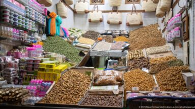 Market stall with mounded dates, nuts, seeds, and dried goods filling bins and shelves.