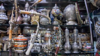 Engraved and pierced metal pitchers, vases, lanterns, and decorative vessels crowded on shop shelves.
