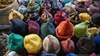 Rows of brightly colored knit or woven caps in striped and mottled yarn patterns.