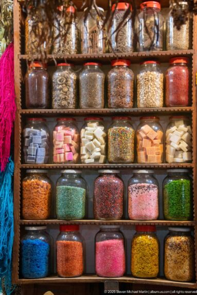 Glass jars arranged on shelves and filled with colorful beads, flakes, and small decorative materials.