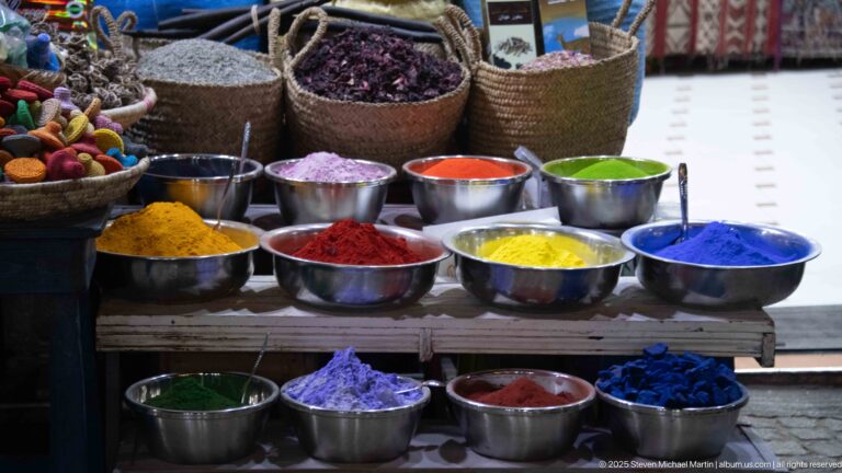 Metal bowls filled with vivid colored powders in blue, green, red, yellow, purple, and pink.
