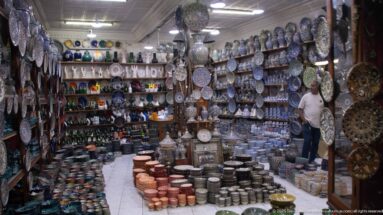 Long craft shop filled with painted pottery, metal trays, bowls, pots, and decorative vessels.