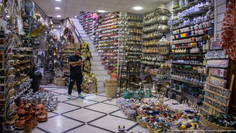 Bright shop interior with lamps, pottery, metal crafts, and rows of colorful souvenir goods.