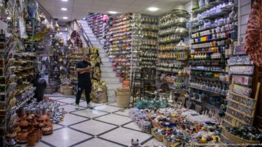 Bright shop interior with lamps, pottery, metal crafts, and rows of colorful souvenir goods.