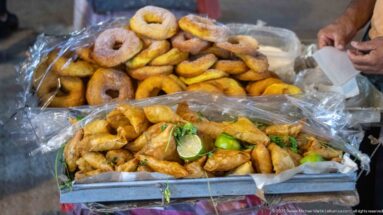 Tray of fried triangular pastries with lime and herbs below a pile of ring-shaped breads.
