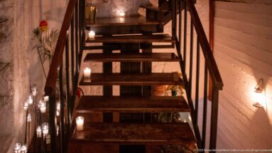 Dark wooden staircase with open treads and small candles glowing along the walls and steps.