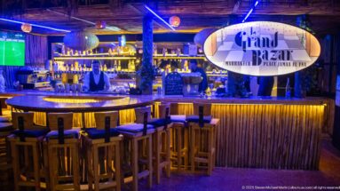 Grand Bazar Marrakech bar with illuminated sign, wooden stools, and bottle shelves.