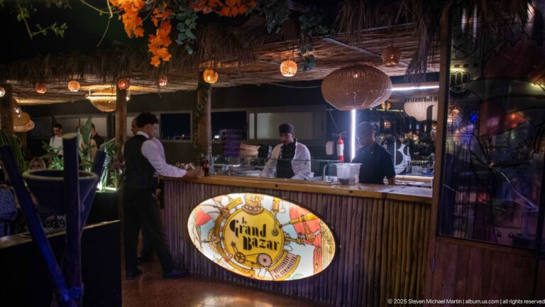 Staff working behind the Grand Bazar bar counter beneath hanging lights.