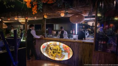 Staff working behind the Grand Bazar bar counter beneath hanging lights.