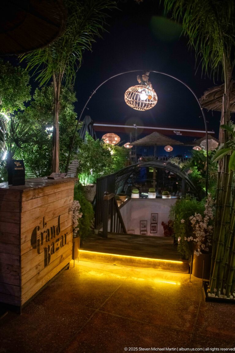 Night entrance to Grand Bazar with glowing steps, plants, and dark timber railings.