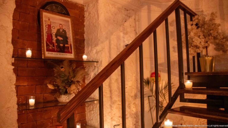 Wooden staircase beside brick and plaster walls with framed art, candles, and flowers.