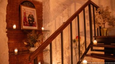 Wooden staircase beside brick and plaster walls with framed art, candles, and flowers.