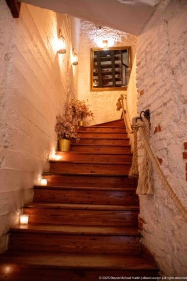 Wide wooden staircase with rope handrail, pale textured walls, and small candles.