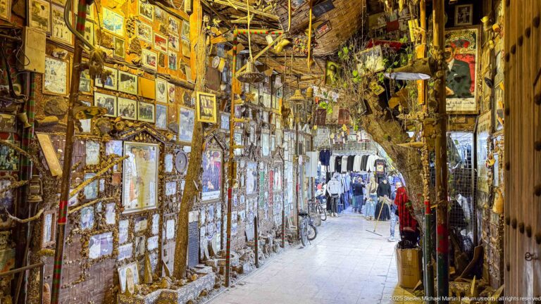Narrow passage densely covered with framed pictures, mirrors, and hanging decorative objects.