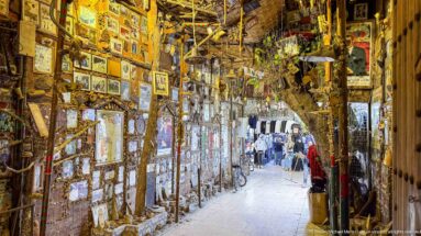 Narrow passage densely covered with framed pictures, mirrors, and hanging decorative objects.