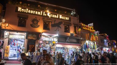Night view of Restaurant Le Grand Bazar above bright shops and a crowded pedestrian street.