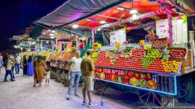 Bright juice stall No. 20 piled with colorful fruit as two customers stand at the counter in Jemaa el-Fna.