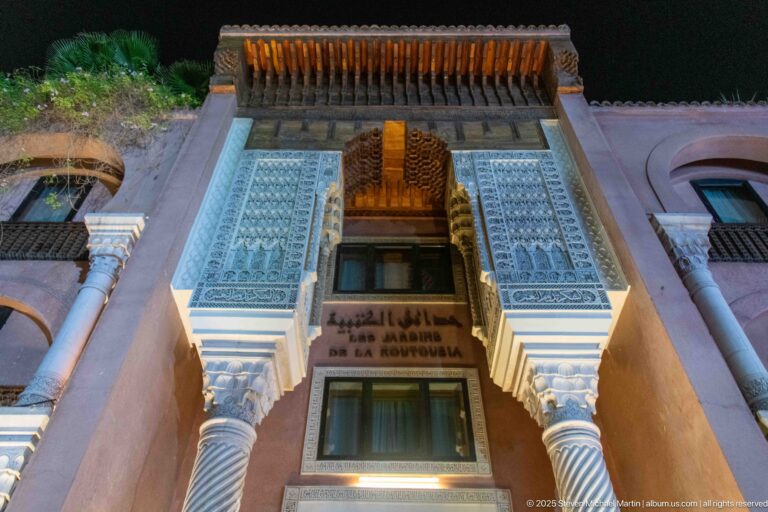 Ornate façade with carved plaster, twisted columns, wooden canopy, and bilingual sign above a doorway.