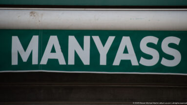 Close view of a green rectangular sign with white capital letters reading MANYASS.