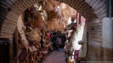 Narrow brick-arched market passage lined with hanging palm-fiber bags, mats, and woven goods.