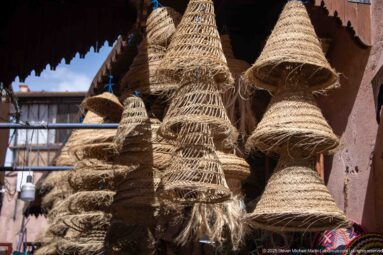 Cluster of large conical woven straw or palm-fiber lampshades hanging above a market stall.