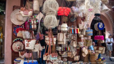 Market shopfront densely hung with straw bags, baskets, fringed pieces, and colorful woven accessories.