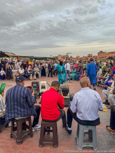 Elevated view over seated men and dense crowds gathering across Djemaa El Fna.