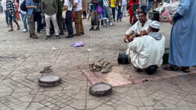 Two seated street performers with drums and round covered baskets on the pavement at Djemaa El Fna.