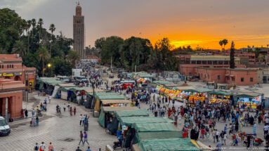 Rows of Djemaa El Fna market stalls and pedestrians beneath a vivid orange sunset.