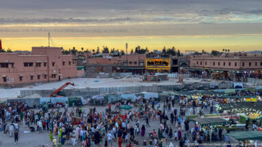 Elevated dusk view across Djemaa El Fna with crowds, market stalls, and low medina buildings.