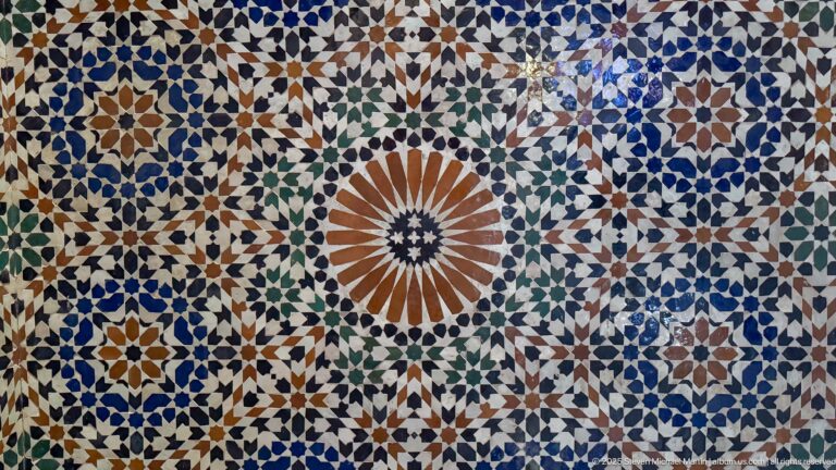 Close-up of multicolored zellij with a large central sunburst rosette surrounded by smaller geometric stars.