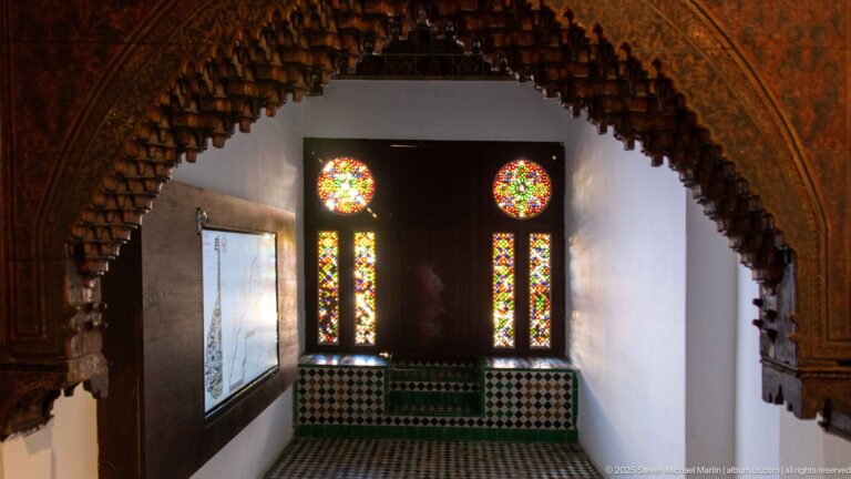 Two circular stained-glass rosettes above tall colored-glass panels, framed by carved wood and zellij.