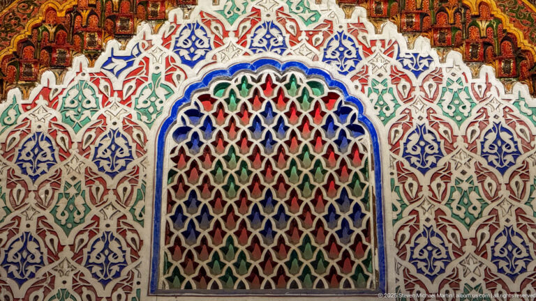 Arched multicolored lattice niche surrounded by dense carved plaster ornament in blue, green, red, and white.