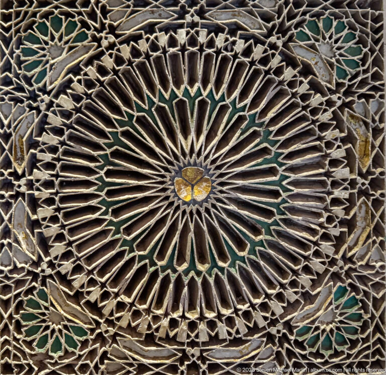 Close-up of a pale radial lattice rosette with many spokes, nested geometric bands, and a small central floral boss.