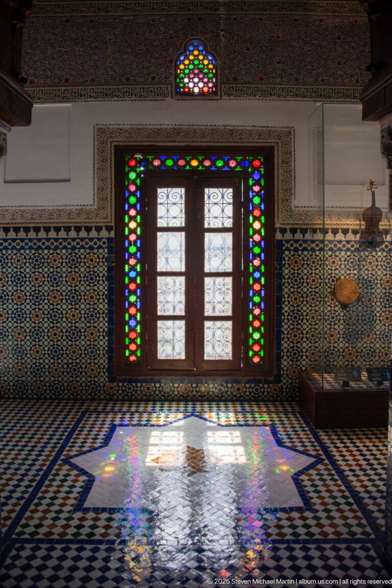Wooden doorway with multicolored glass casting bright colored reflections across a zellij floor.