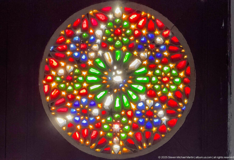 Close-up of a circular stained-glass rosette with red, green, blue, amber, and white geometric pieces.