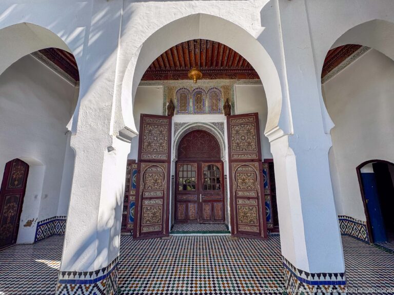 White arcade arches framing a painted wooden doorway across a patterned tile floor.