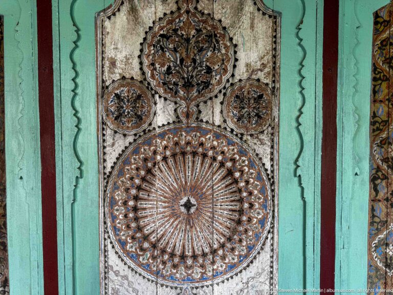 Weathered wooden panel with large circular sunburst, three floral medallions, and turquoise framing.