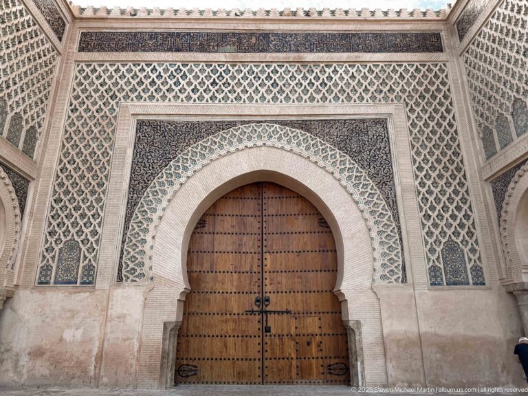 Centered studded wooden doors framed by a pale horseshoe arch and patterned green façade.