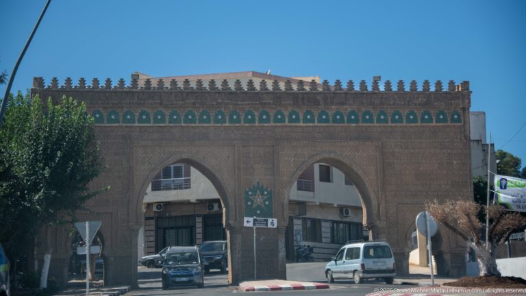 Twin-arched masonry gateway with crenellated roofline, central star motif, and cars passing beneath.