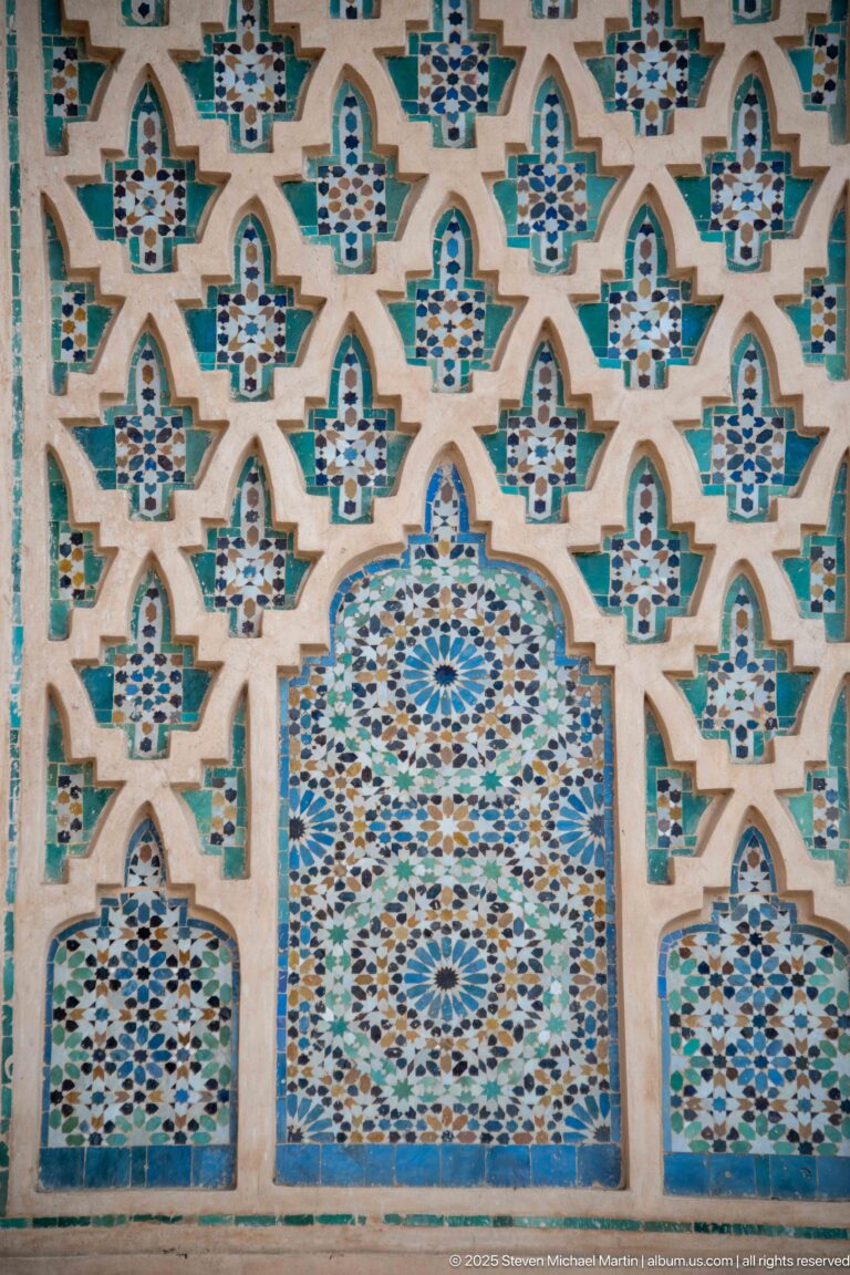 Close-up of multicolored geometric mosaic panels with star and rosette patterns in arched compartments.