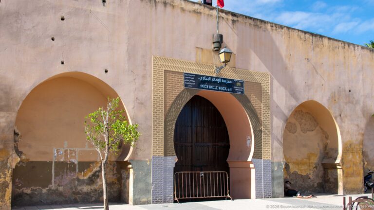Dark arched doorway with a bilingual sign and patterned border, flanked by larger blind arches.