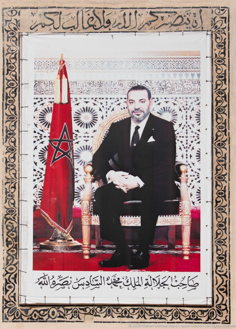 Framed official portrait of King Mohammed VI seated beside the red Moroccan flag.